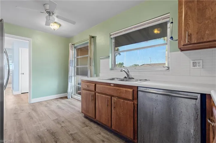 Kitchen with decorative backsplash, a ceiling fan, light wood-type flooring, dishwasher, and a sink