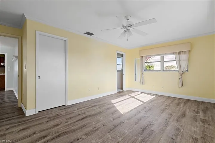 Unfurnished bedroom with crown molding, baseboards, visible vents, and wood finished floors