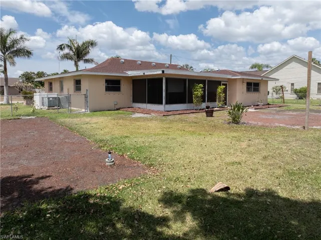 Rear view of property with fence, stucco siding, a sunroom, a gate, and a lawn
