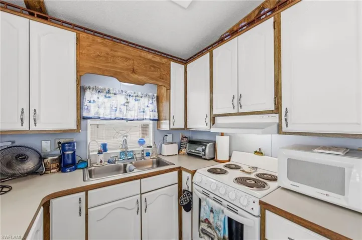 Kitchen featuring white cabinets, white appliances, light countertops, and a textured ceiling