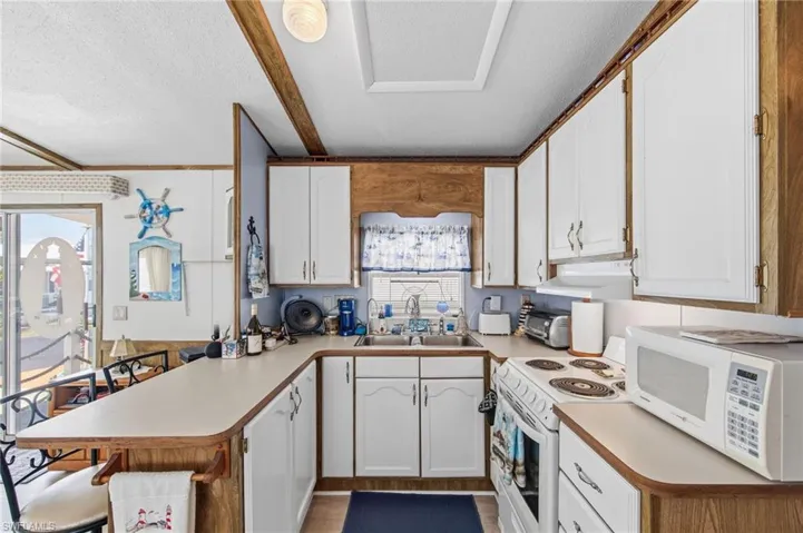 Kitchen featuring white cabinetry, a peninsula, white appliances, a textured ceiling, and light countertops