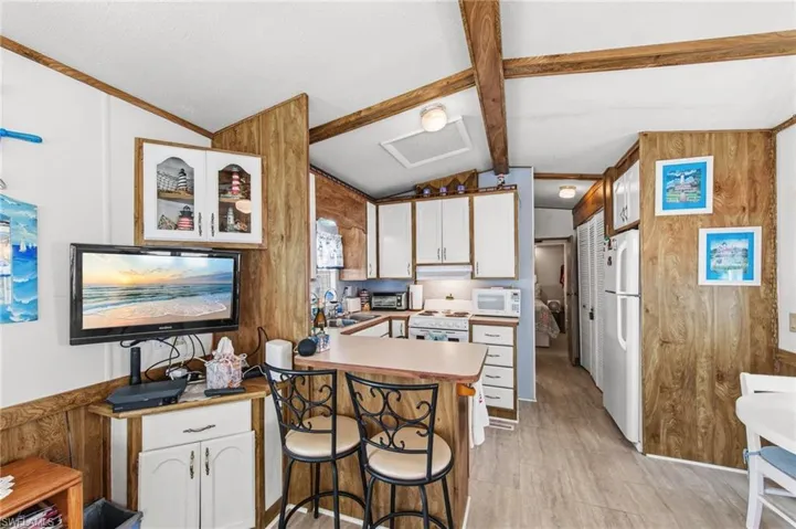 Kitchen featuring wooden walls, white cabinetry, a peninsula, a kitchen breakfast bar, and white appliances