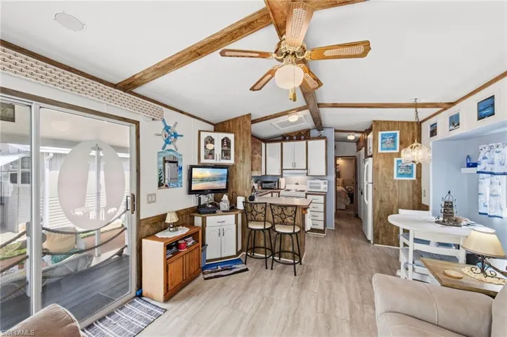 Dual tone kitchen with a breakfast bar, lofted ceiling with beams, white appliances, ceiling fan, and a peninsula