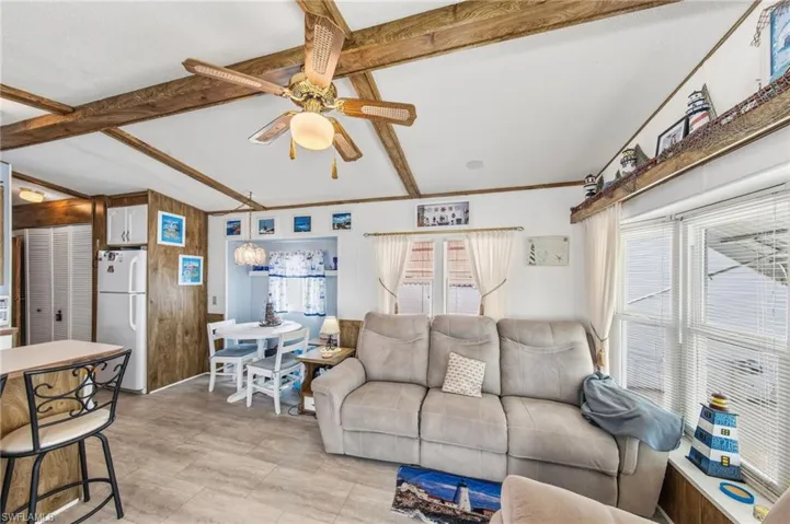Living room featuring a ceiling fan, lofted ceiling with beams, and wooden walls