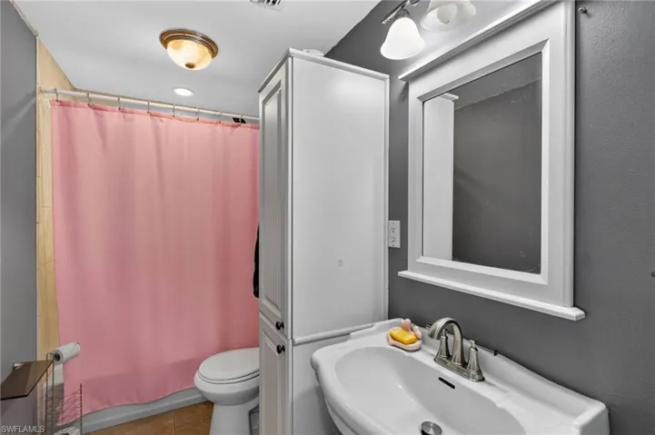 Bathroom featuring a pedestal sink, framed mirror, built-in storage cabinet, and tiled shower surround