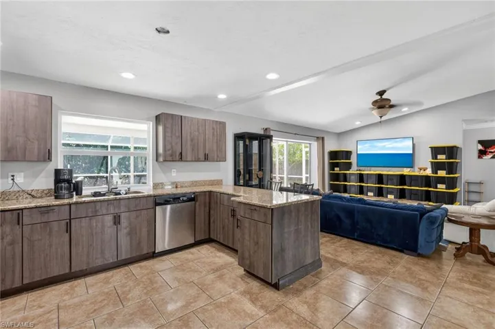 Open-concept kitchen and living area featuring wood-finish cabinetry, stainless steel appliances, and granite countertops