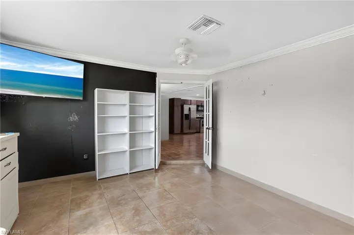 Tiled flooring throughout this versatile room, featuring crown molding, a ceiling fan, and French doors