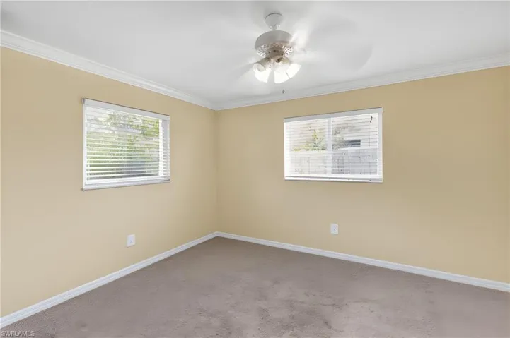 Carpeted room featuring two windows with horizontal blinds, a ceiling fan with integrated lighting, and crown molding