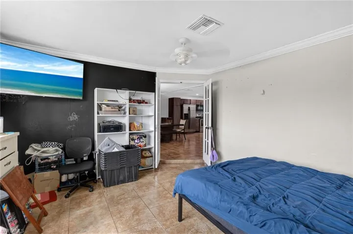 Tiled flooring throughout this room, featuring crown molding, a ceiling fan, and French doors