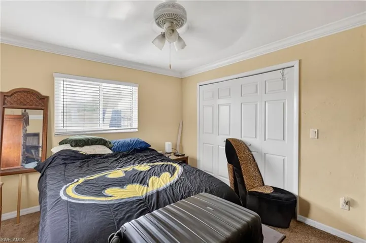 Carpeted bedroom featuring a double window with blinds, a ceiling fan with integrated lighting, white bi-fold closet doors, and crown molding