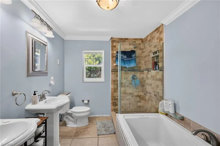 Spacious bathroom featuring a glass-enclosed shower with stone tile surround, a separate soaking tub, and a pedestal sink