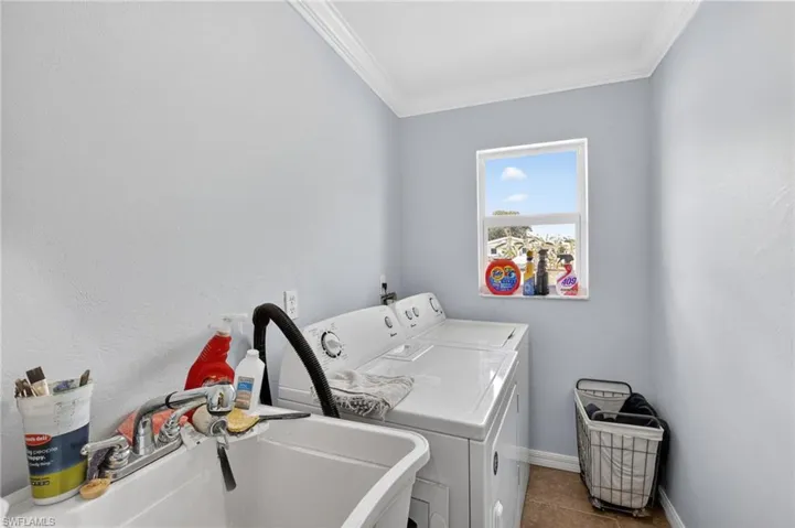 Dedicated laundry room featuring a utility sink with a chrome faucet, light blue walls, crown molding, and tiled flooring