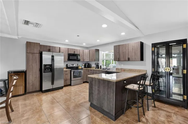 Kitchen featuring a central island with countertop seating, wood-finish cabinetry, stainless steel appliances, and tiled flooring