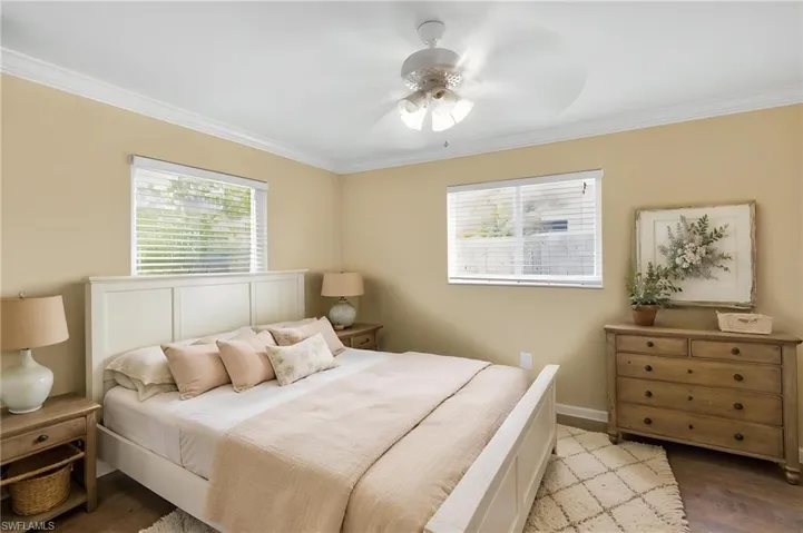 Bedroom featuring crown molding, two windows with blinds, a ceiling fan, and wood-finish flooring