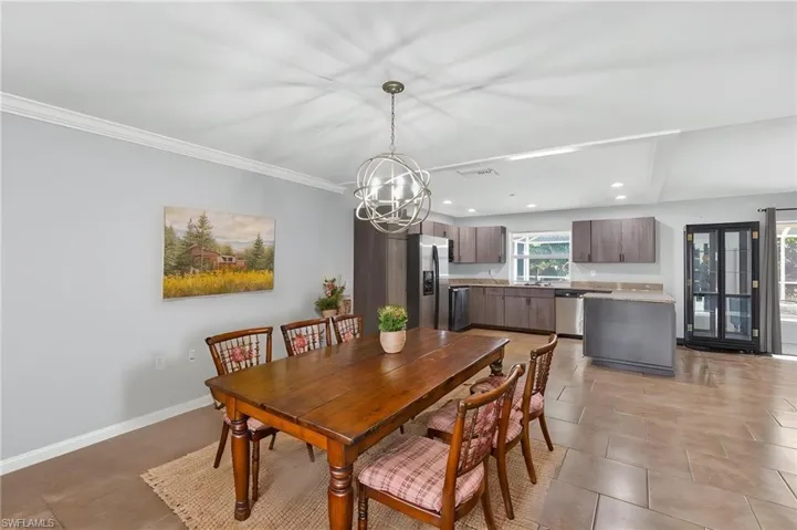 Open-concept living space featuring a dining area with a contemporary orb chandelier, crown molding, and large format tile flooring