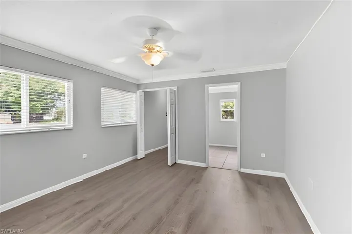 Spacious room featuring wood-finish flooring, light gray walls, and crown molding
