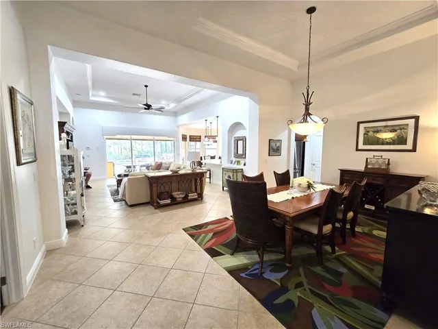 Tiled dining room with a raised ceiling, ceiling fan, and ornamental molding