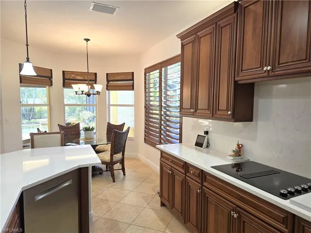 Kitchen with decorative light fixtures, black electric stovetop, plenty of natural light, and a notable chandelier in breakfast nook