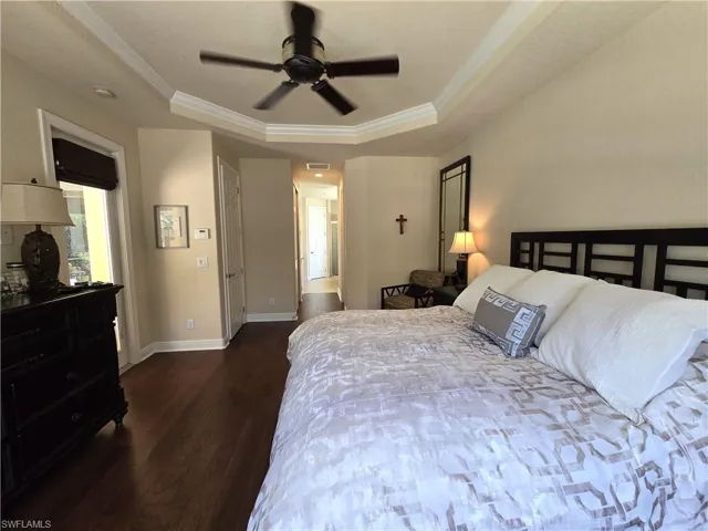 Bedroom featuring a tray ceiling, dark hardwood / wood-style flooring, ornamental molding, and ceiling fan