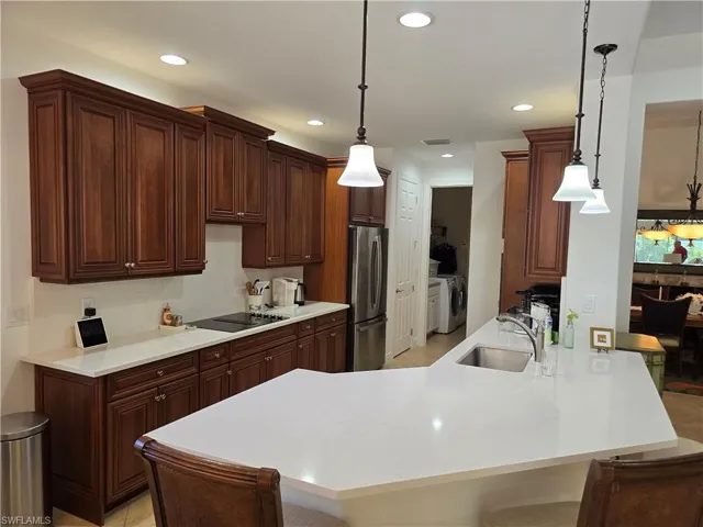 Kitchen featuring a breakfast bar area, stainless steel fridge, washing machine and clothes dryer, kitchen peninsula, and sink