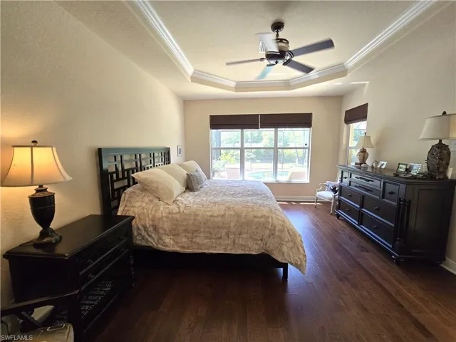Bedroom with ceiling fan, a raised ceiling, dark hardwood / wood-style flooring, and crown molding