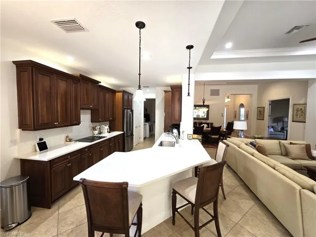 Kitchen cherry wood  cabinetry, hanging light fixtures, stainless steel refrigerator, and a breakfast bar