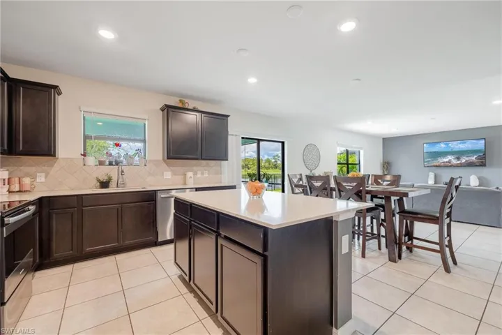 Kitchen featuring dark brown cabinetry, backsplash, a center island, appliances with stainless steel finishes, and light tile floors