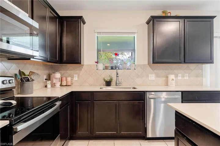 Kitchen featuring appliances with stainless steel finishes, sink, tasteful backsplash, and light tile floors