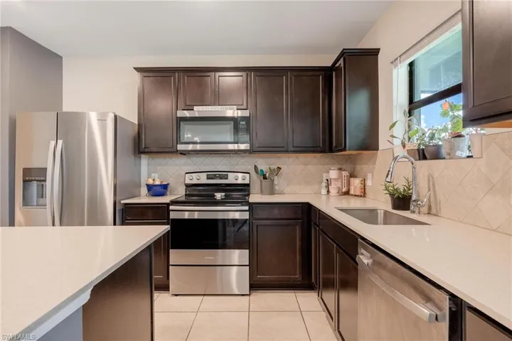 Kitchen featuring dark brown cabinetry, backsplash, light tile floors, sink, and appliances with stainless steel finishes