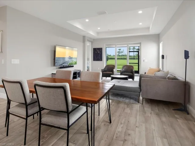 Open-concept living area featuring wood-finish flooring, a tray ceiling with recessed lighting, and expansive glass doors opening to green space