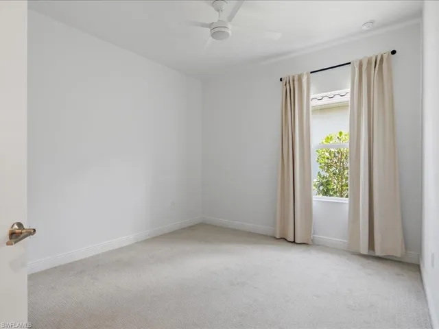 Carpeted interior room featuring a window with natural light, a ceiling fan, and white baseboards