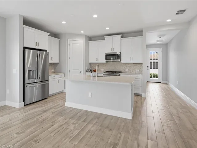 Kitchen featuring white cabinetry, stainless steel appliances, a center island with sink, and a herringbone pattern tile backsplash