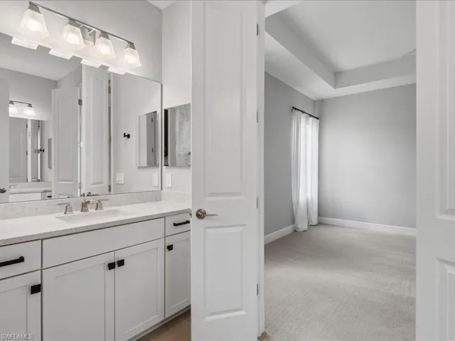Bathroom vanity with double sinks, light-toned countertop, white cabinetry with black hardware, and a four-light fixture