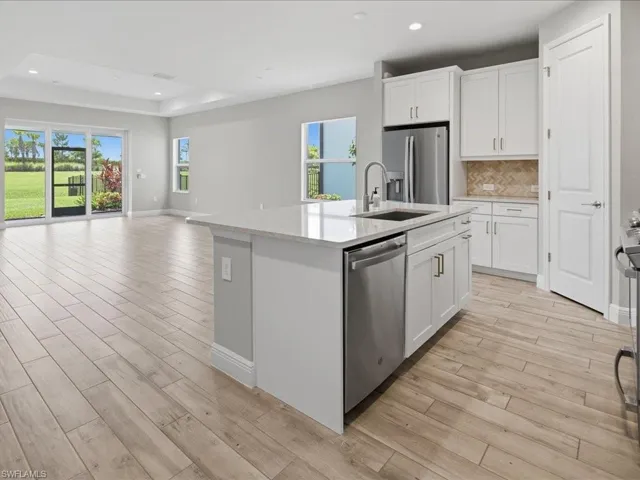 Open-concept kitchen and living area featuring a large center island with a sink, white cabinetry with brushed nickel hardware, and stainless steel appliances