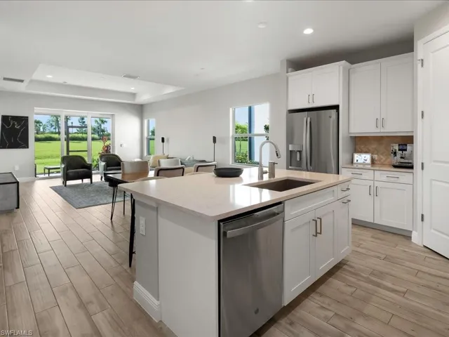 Open-concept kitchen featuring a central island with an undermount sink, light-toned countertop, and white shaker-style cabinetry