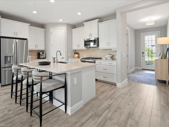 Contemporary kitchen featuring white shaker cabinetry, stainless steel appliances, a center island with sink, and wood-finish flooring