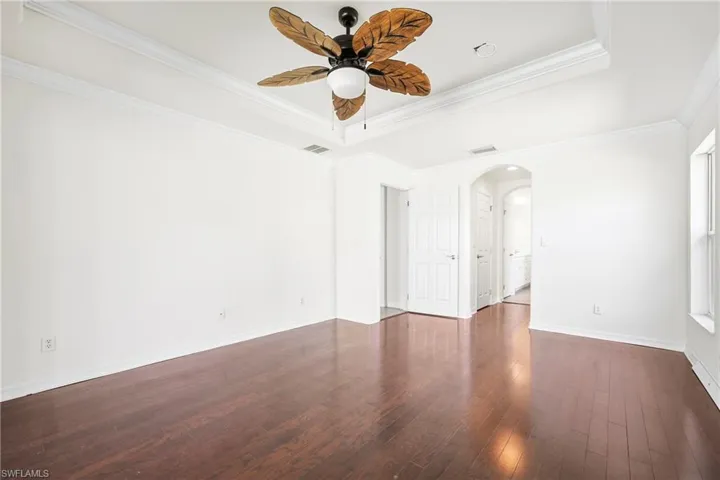 Spacious interior featuring wood-finish flooring, a tray ceiling with crown molding, and a tropical-inspired ceiling fan