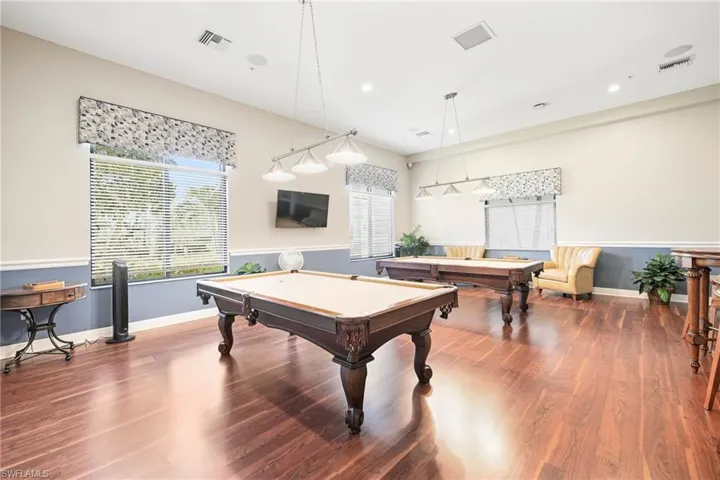 Spacious recreation room featuring rich wood-finish flooring, multiple windows with blinds, a chair rail, and recessed lighting