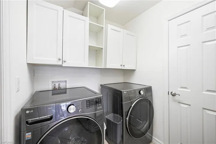 Dedicated laundry area featuring white shaker-style cabinetry, open shelving, a paneled interior door, and light-toned wall finishes
