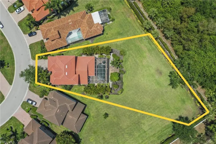 Aerial perspective showcasing a property with a terracotta tile roof, screened swimming pool, and a paved driveway