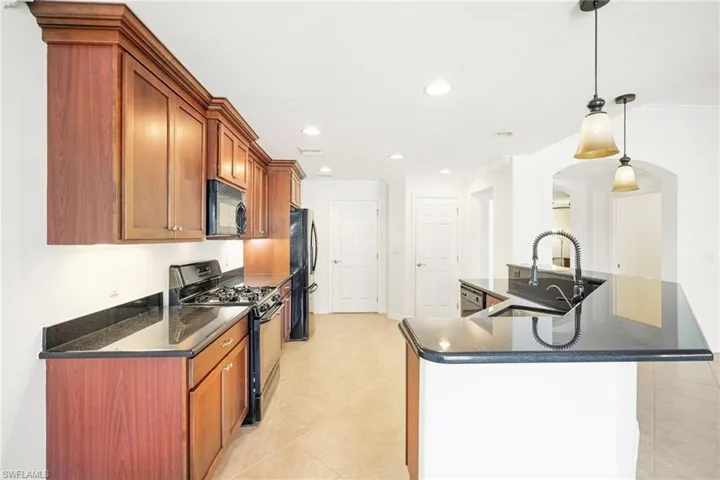 Kitchen featuring dark wood-finish cabinetry, black appliances, black countertops, and a central island with a gooseneck faucet