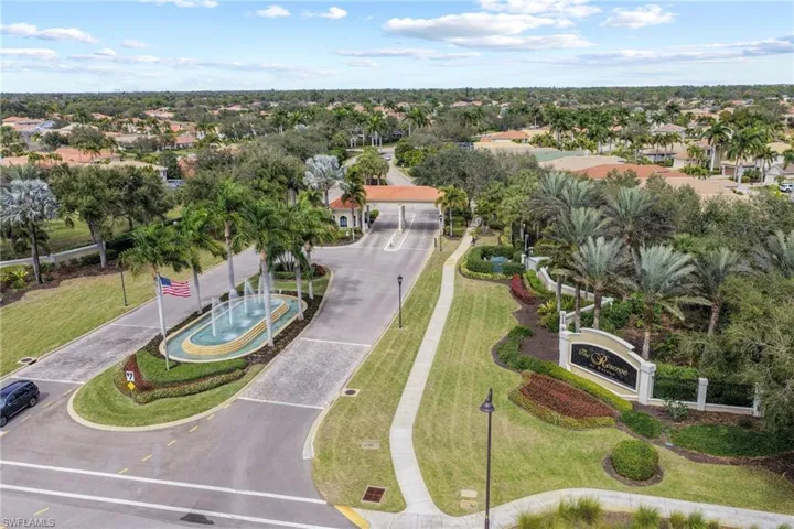 Gated community entrance featuring a decorative fountain centerpiece, extensive tropical landscaping, and a grand entry sign
