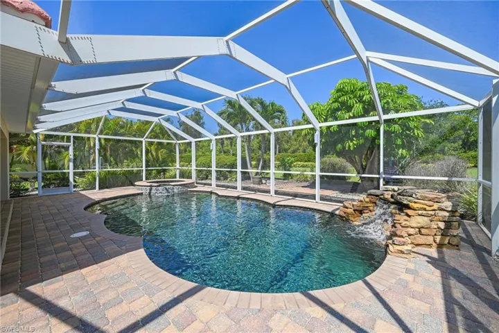 Screened-in outdoor pool area featuring a freeform pool with a stone waterfall, integrated spa, and paver decking