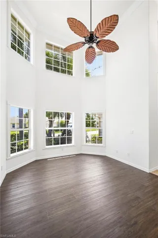Two-story interior space featuring wood-finish flooring, multiple windows providing natural light, a ceiling fan with leaf-shaped blades, and white walls