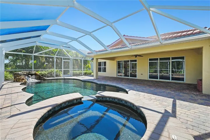 Screened outdoor living area featuring a freeform pool with a rock waterfall feature, an integrated spa, and a paver patio