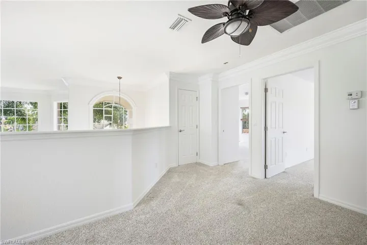 Carpeted upper-level space featuring a contemporary ceiling fan, multiple doorways, and a half-wall overlooking a lower area with arched and rectangular windows