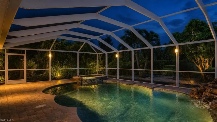 Screened pool enclosure featuring an integrated spa, a custom rock waterfall, and paver decking
