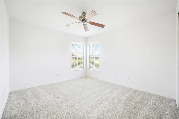Room featuring light-toned carpeting, white walls, and a corner window arrangement with white louvered blinds