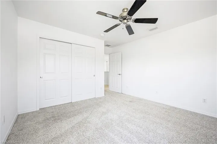 Spacious room featuring light-toned carpeting, white walls, and a ceiling fan with integrated lighting