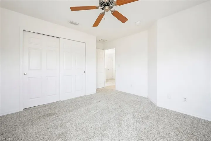 Spacious room featuring light-colored carpeting, white painted walls, a ceiling fan with wood-finish blades, and sliding bifold closet doors